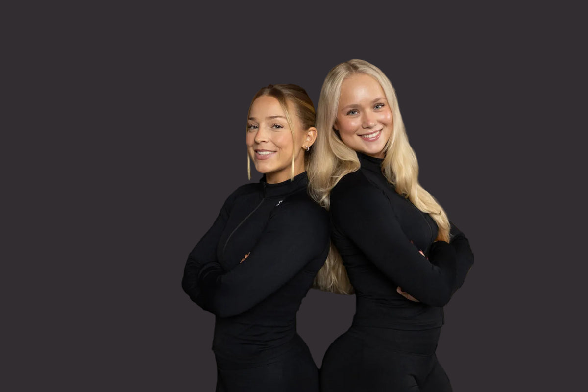 Two women in black outfits standing against a striped brown background
